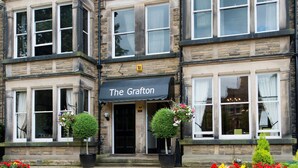 A building with a sign reading "The Grafton" and a paved entrance area with flower beds. - The Grafton (Harrogate)