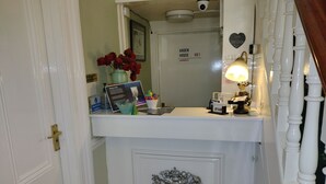 A reception desk with a vase of red roses, a framed picture, a sign reading "Jardim House Harrogate," and a coat rack with a lamp. - Arden House (Harrogate)