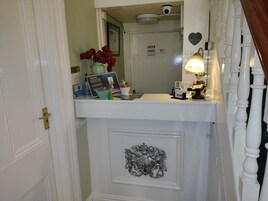 A reception desk with a vase of red roses, a framed picture, a sign reading "Jardim House Harrogate," and a coat rack with a lamp.