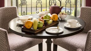 A dining table with a fruit bowl, teapot, and cups, set in a room with patterned chairs and a view of a park through a glass door. - West Park Hotel (Harrogate)