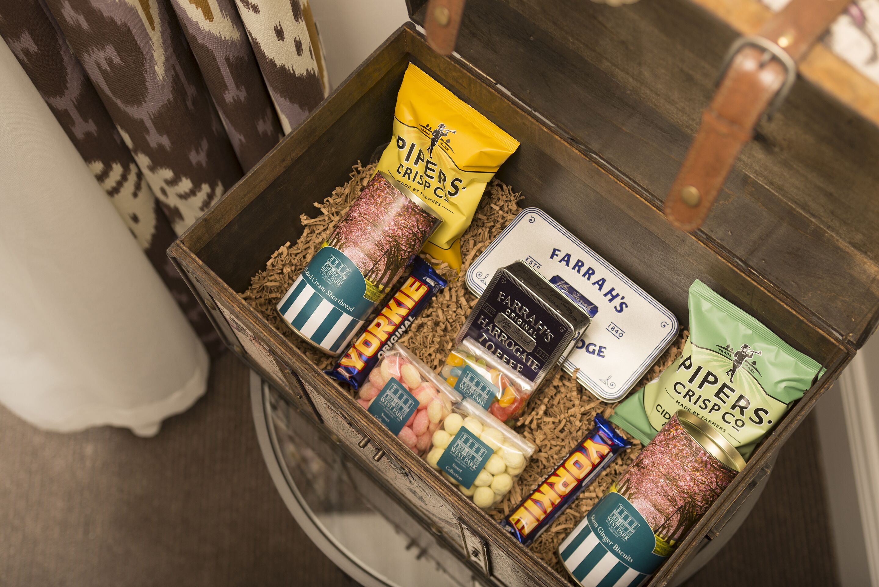 A wooden box filled with various food items including snacks and beverages.