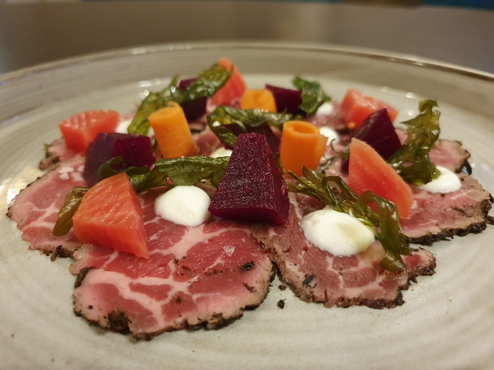 A plate of sliced meat with vegetables and a creamy sauce.