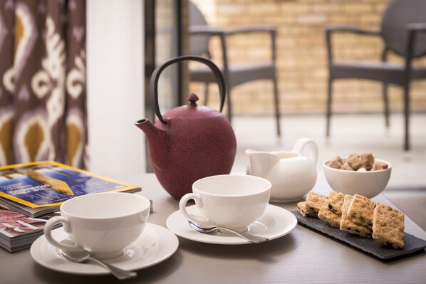 A table with a teapot, cups, a bowl of cookies, and a magazine.