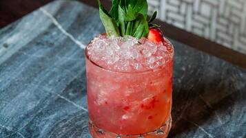 A cocktail with ice and a strawberry garnish on a slate coaster.