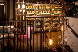 A bar area with a wooden railing, a seating area with a pink chair, and a decorative light fixture with leaf-shaped elements.