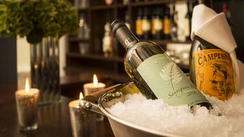 A bottle of wine in a bucket of ice, a candle, and a vase of flowers on a bar counter.