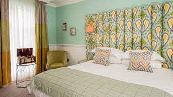 A neatly arranged hotel room with a bed, a chair, a small table with a lamp, and curtains.