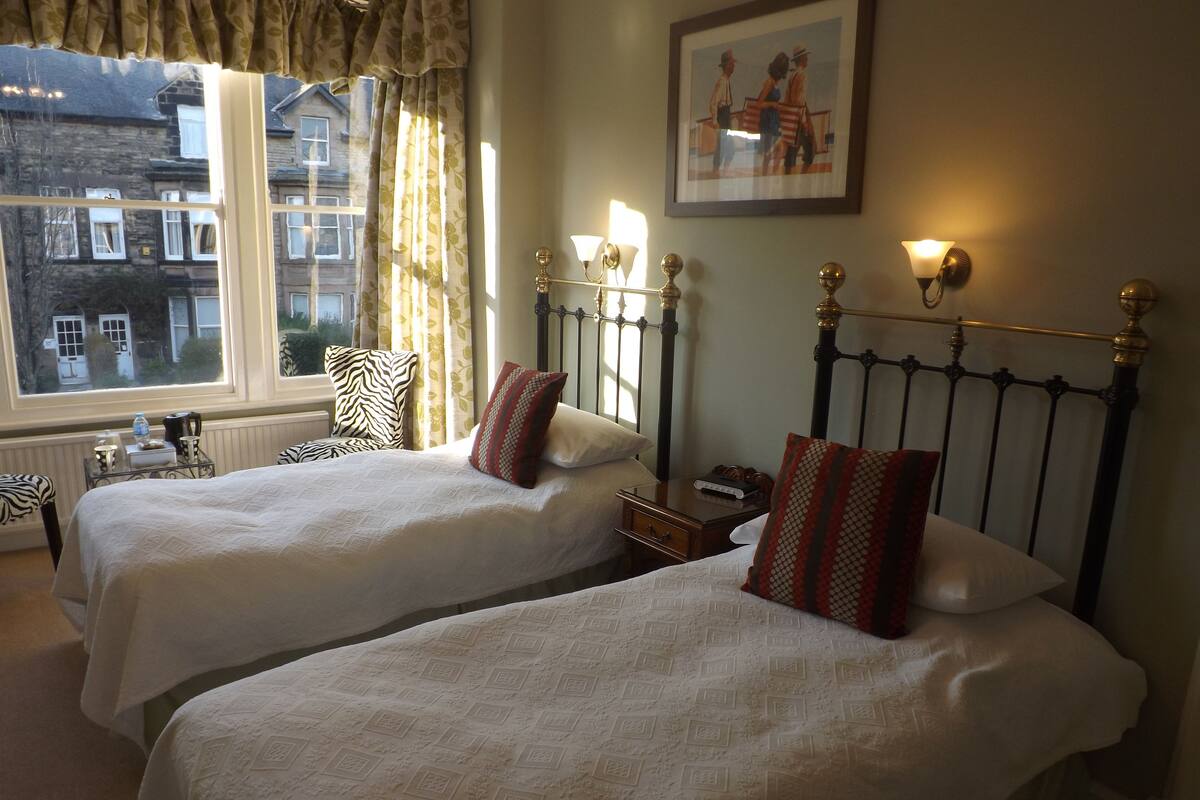 A hotel room with two beds, a window with curtains, a framed picture on the wall, and bedside lamps.