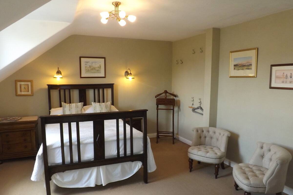 A bedroom with a bed, two chairs, a dresser, and a hanging coat rack.