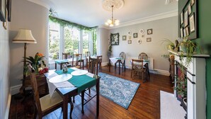 A dining area with a wooden table set for four, surrounded by chairs. There is a chandelier above the table, and the room has a green accent wall with framed pictures. - Wynnstay House (Harrogate)