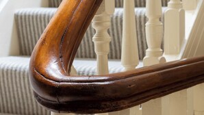 A wooden handrail with a curved design, white balusters, and striped carpeted steps. - Wynnstay House (Harrogate)