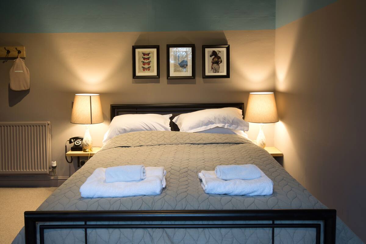 A neatly made bed with two folded towels, two bedside lamps, and three framed pictures on the wall.