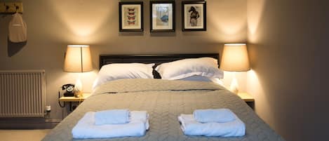 Una cama bien hecha con dos toallas dobladas, dos lámparas de noche y tres cuadros en la pared.