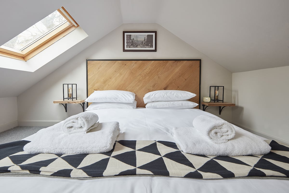 A neatly made bed with white linens and towels, a geometric-patterned throw, and a skylight above.