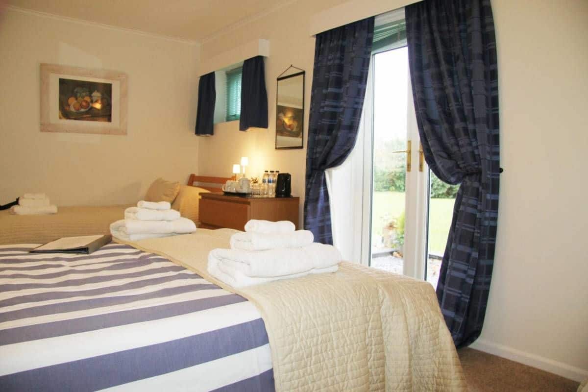 Habitación de hotel con cama, mesita de noche con lámpara, ventana con cortinas y vistas al exterior.