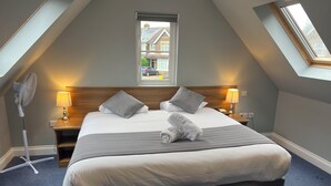 A hotel room with a large bed, two bedside tables with lamps, a standing fan, and a skylight. - The Corner House Hotel Gatwick (Horley)