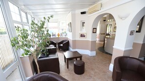 A spacious indoor area with a seating arrangement, a potted plant, and a view through large windows. - The Corner House Hotel Gatwick (Horley)