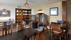 A hotel lobby with a large wooden table, several chairs, a fireplace, a television, and a bookshelf. - The Two Lifeboats (Sheringham)