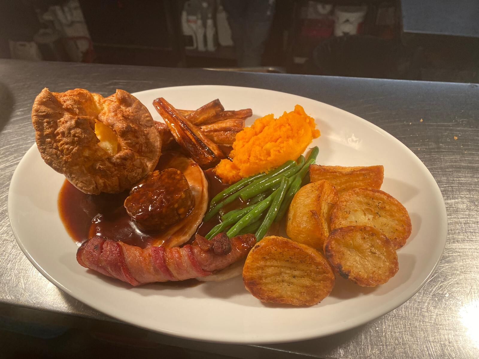 A plate of food including Yorkshire pudding, roast beef, baked beans, mashed sweet potatoes, green beans, and roasted potatoes.