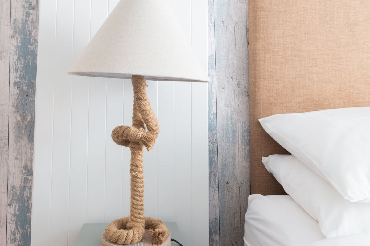 A bed with white bedding, a headboard, and a nightstand with a rope lamp.