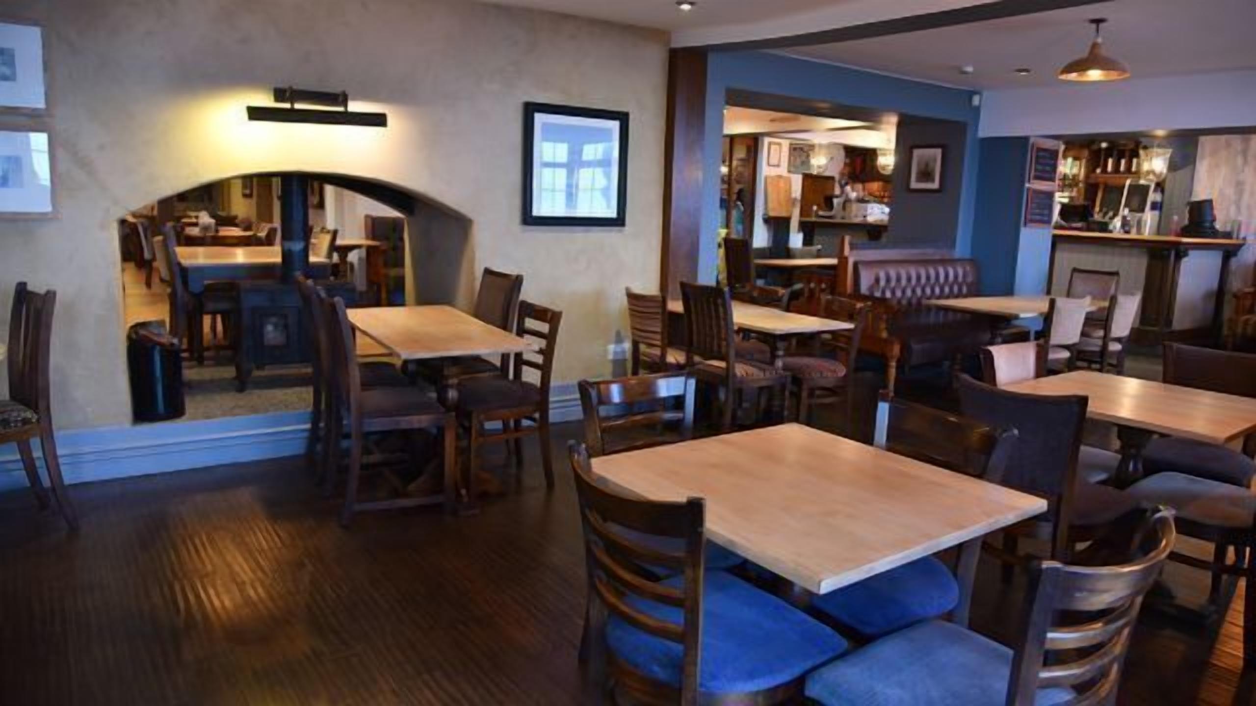 A restaurant with wooden tables and chairs, a bar area, and framed pictures on the walls.