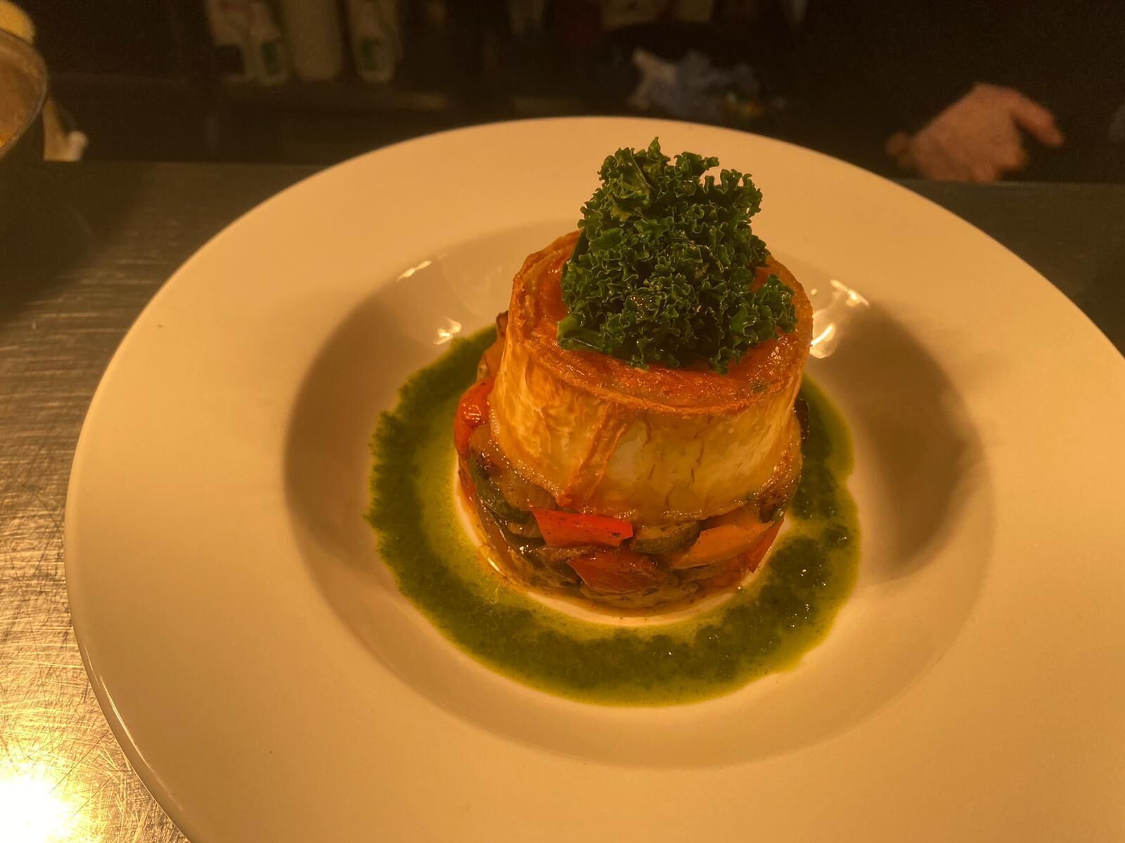 Un plato con un dorado costroso, verduras y una salsa verde sobre un plato blanco.