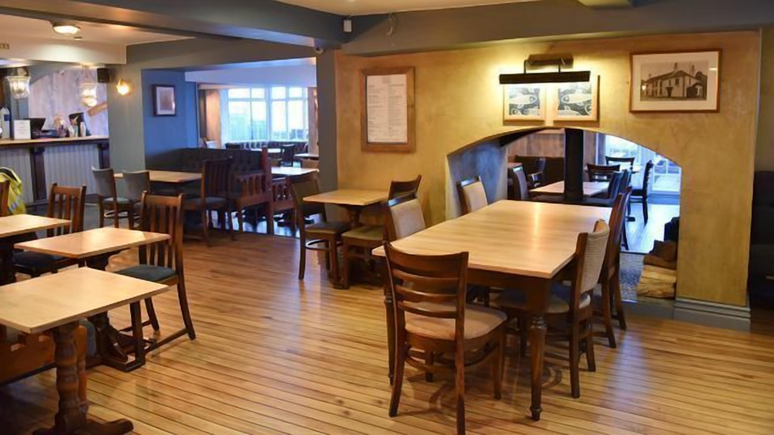 A restaurant with wooden tables and chairs, a bar area, and framed pictures on the walls.