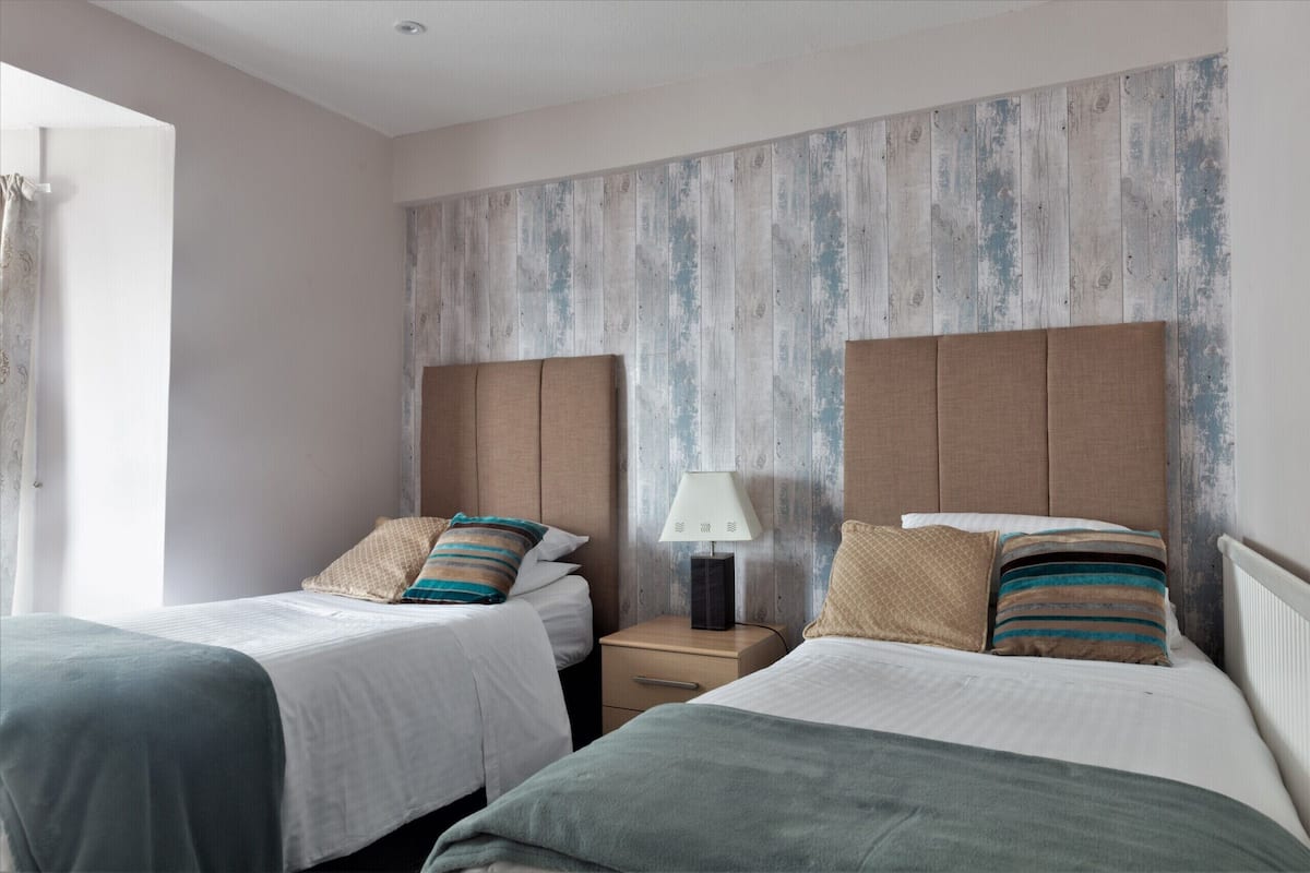 A hotel room with two beds, a nightstand with a lamp, and a wooden wall panel.