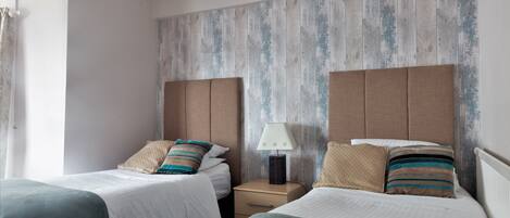 A hotel room with two beds, a nightstand with a lamp, and a wooden wall panel.