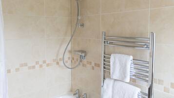 Un baño con bañera, ducha y un perchero con toallas.