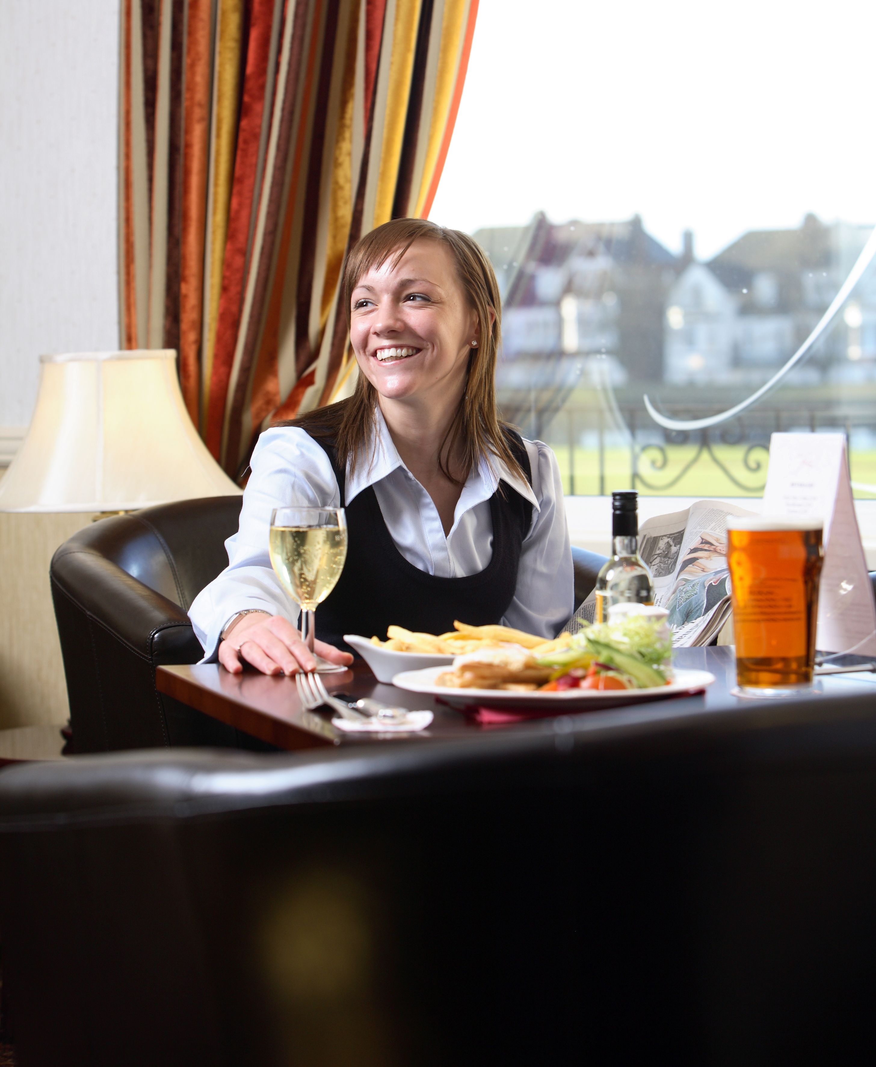 A person seated at a table with a meal, a glass of white wine, and a bottle of beer.