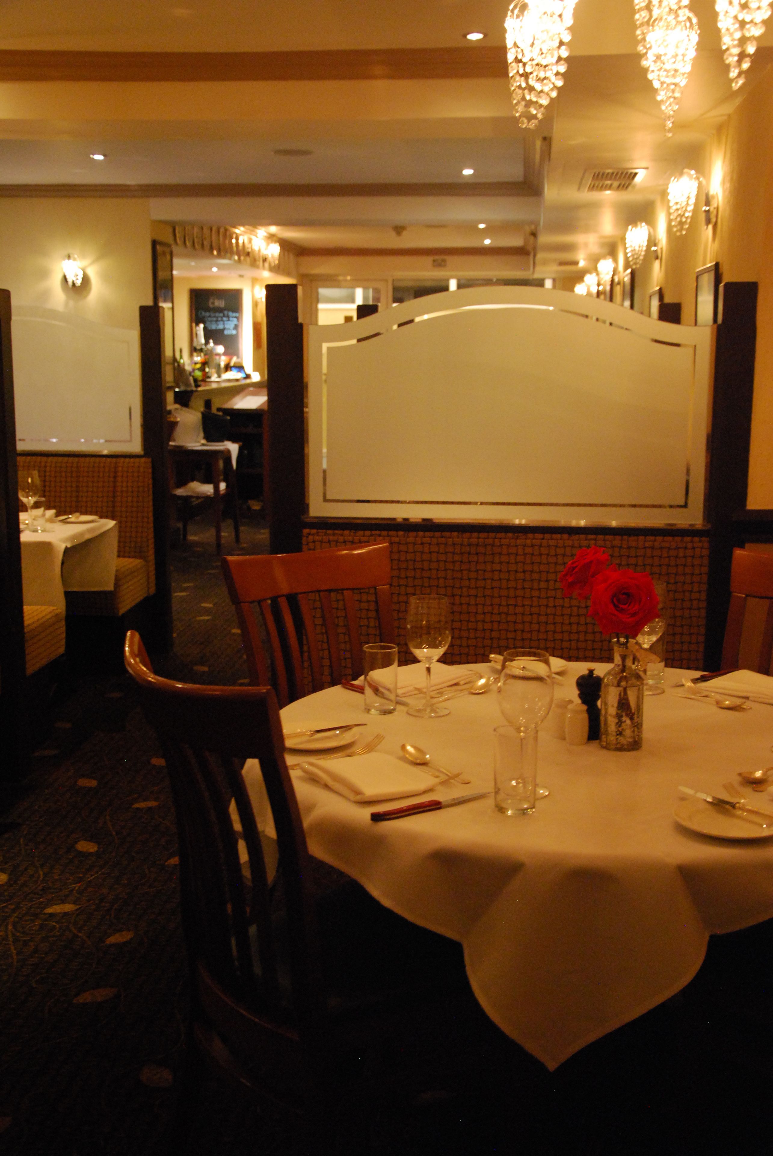 A dining area with a table set for two, a vase with red roses, and a mirror above the table.