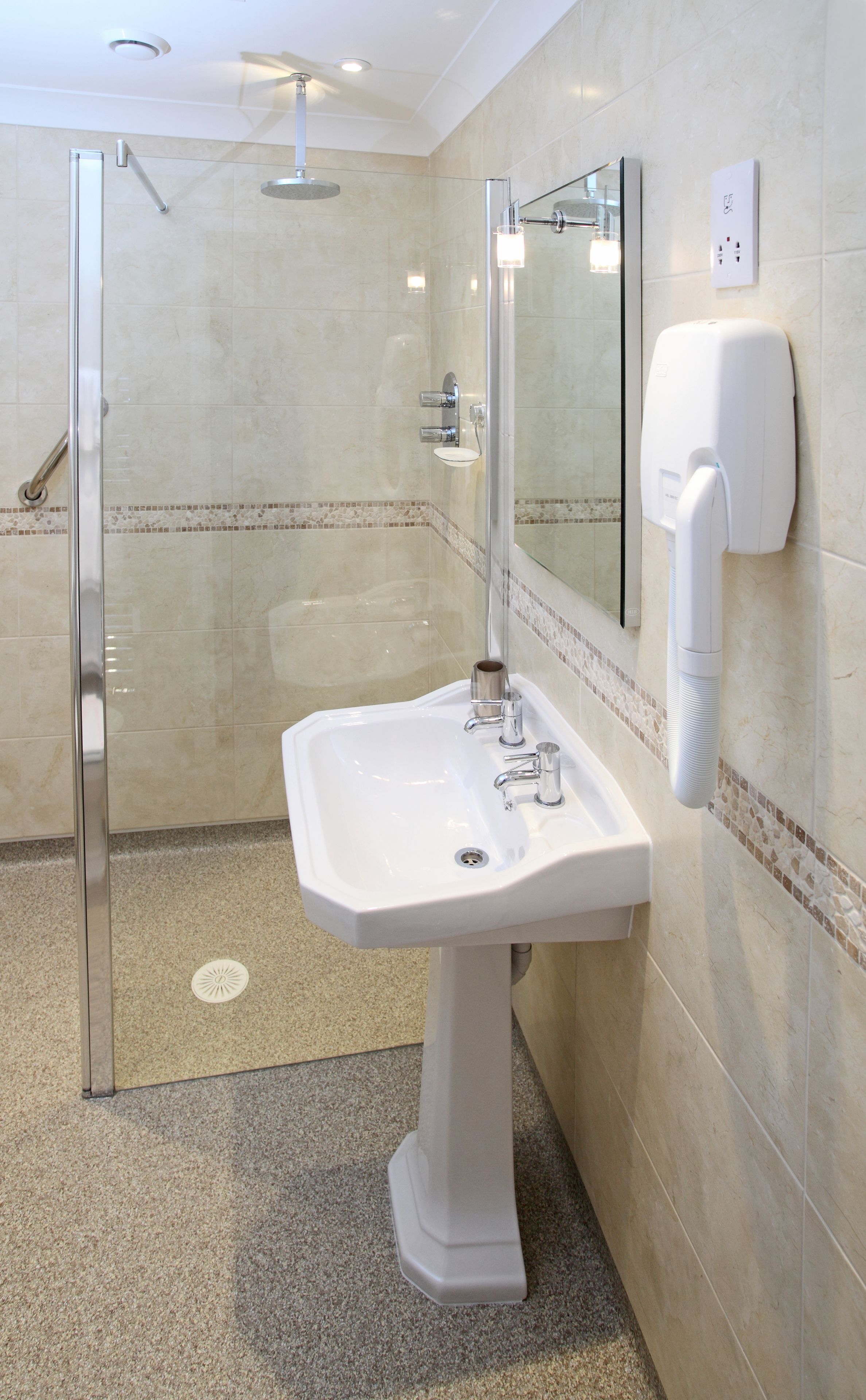 A modern bathroom with a glass-enclosed shower, a pedestal sink, and a hand dryer mounted on the wall.