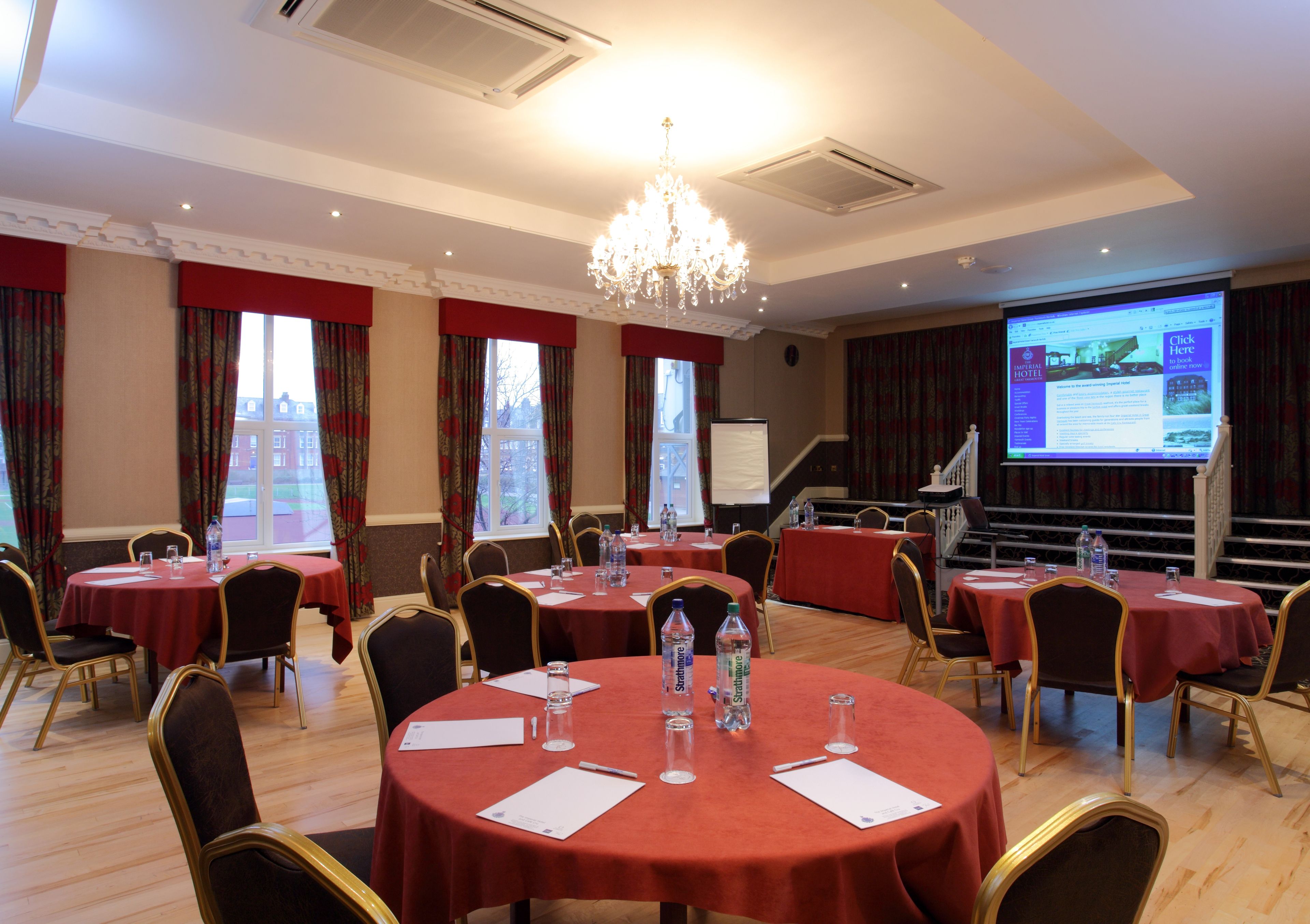 A conference room with round tables, chairs, and a projector screen displaying a webpage.