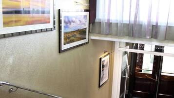 A staircase with a handrail, a chandelier, and framed pictures on the walls.