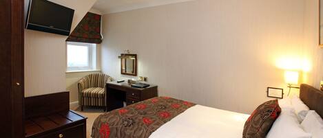 Habitación de hotel con cama, escritorio, silla, televisor montado en la pared y ventana.