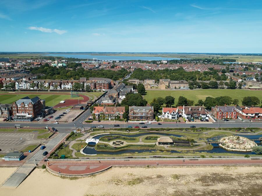 An aerial view of a town with residential areas, a sports field, and a landscaped park with a pond.