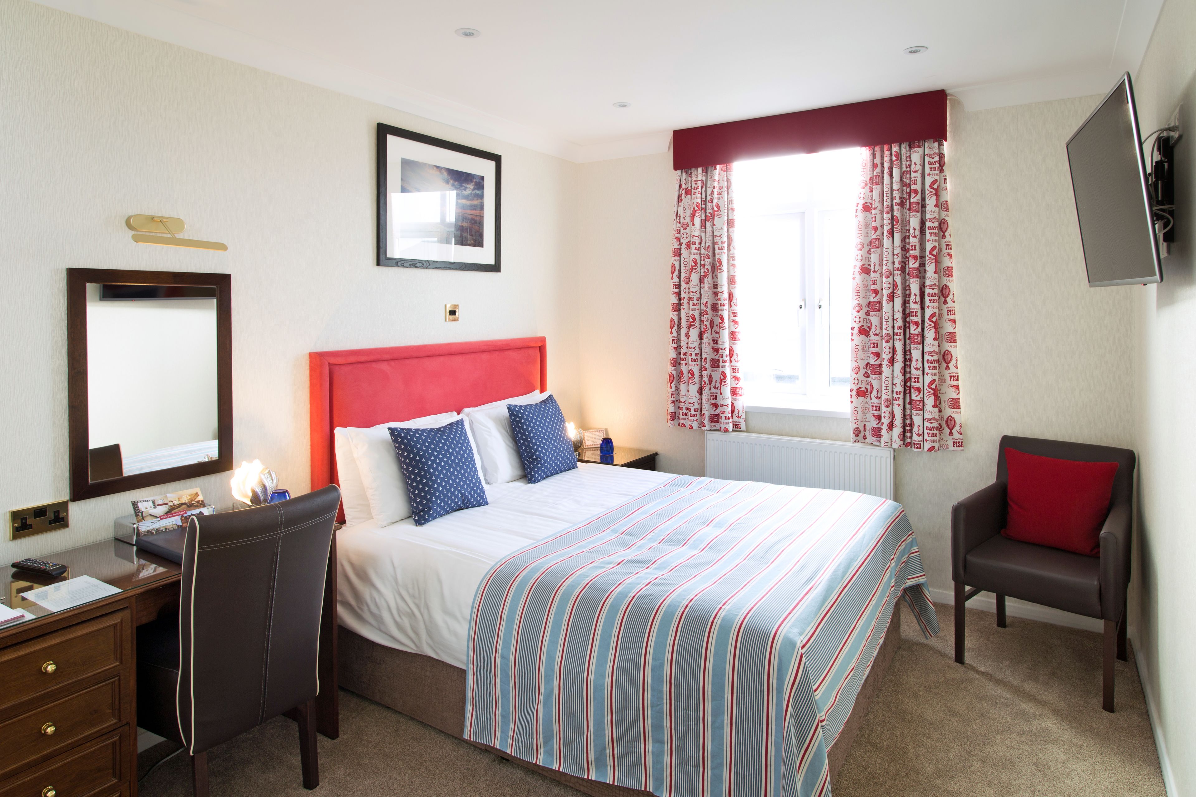 A hotel room with a bed, a desk, a chair, a TV, and a window with curtains.
