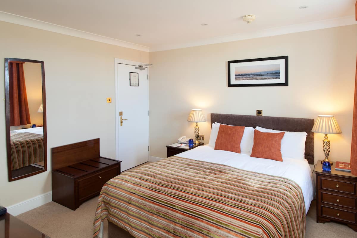 Une chambre d’hôtel comprenant un lit, deux tables de chevet, une commode, un miroir, une porte et un tableau encadré au mur.