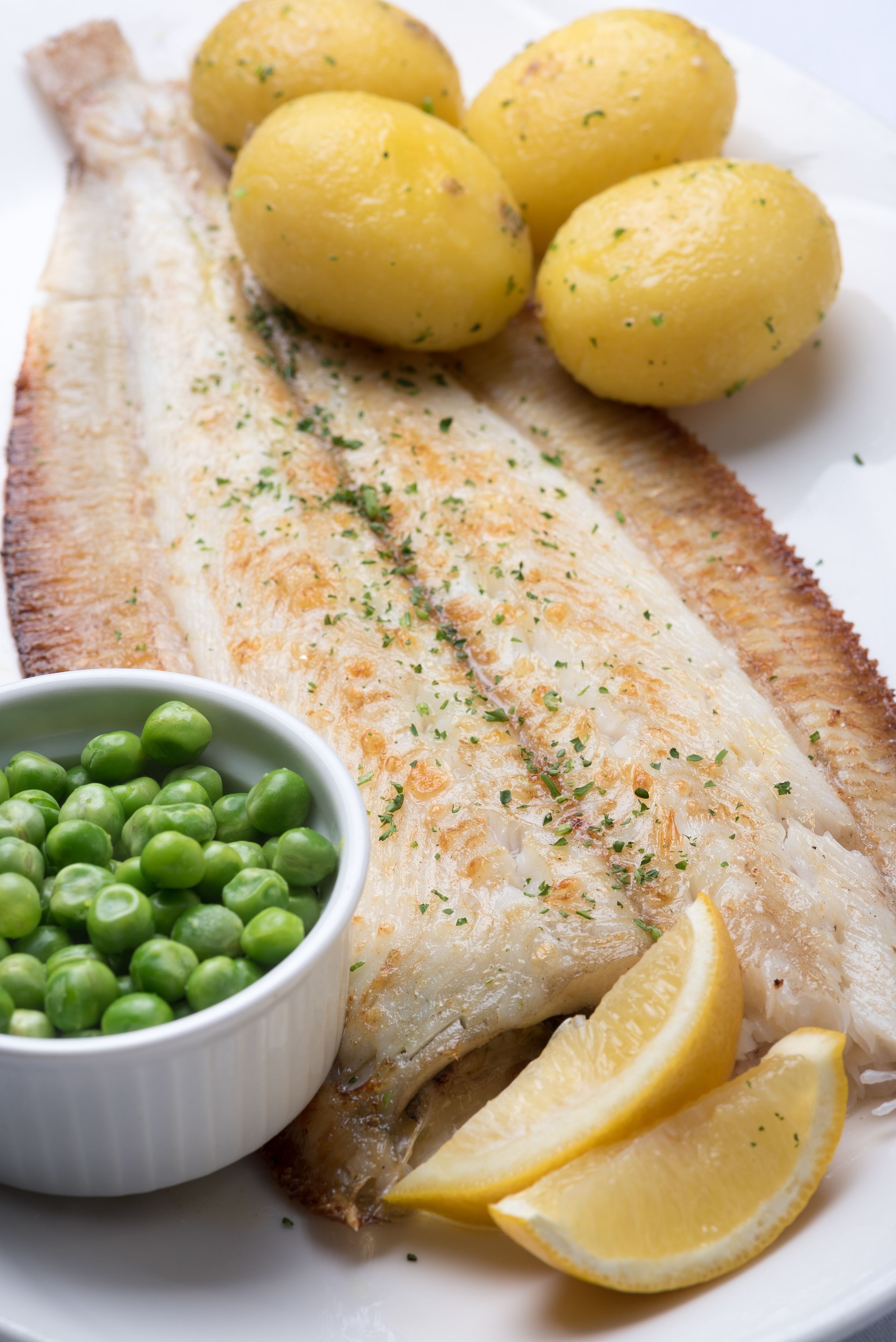 A plate with a whole fish, lemon wedges, and a bowl of peas.