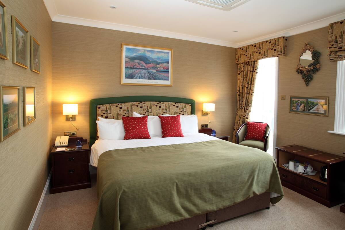 Une chambre d’hôtel avec un grand lit, deux tables de chevet, une petite table, une commode et un tableau au mur.
