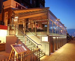 A glass-fronted terrace restaurant with outdoor seating, a staircase leading to the entrance, and a sign indicating the name 'The Terrace'.