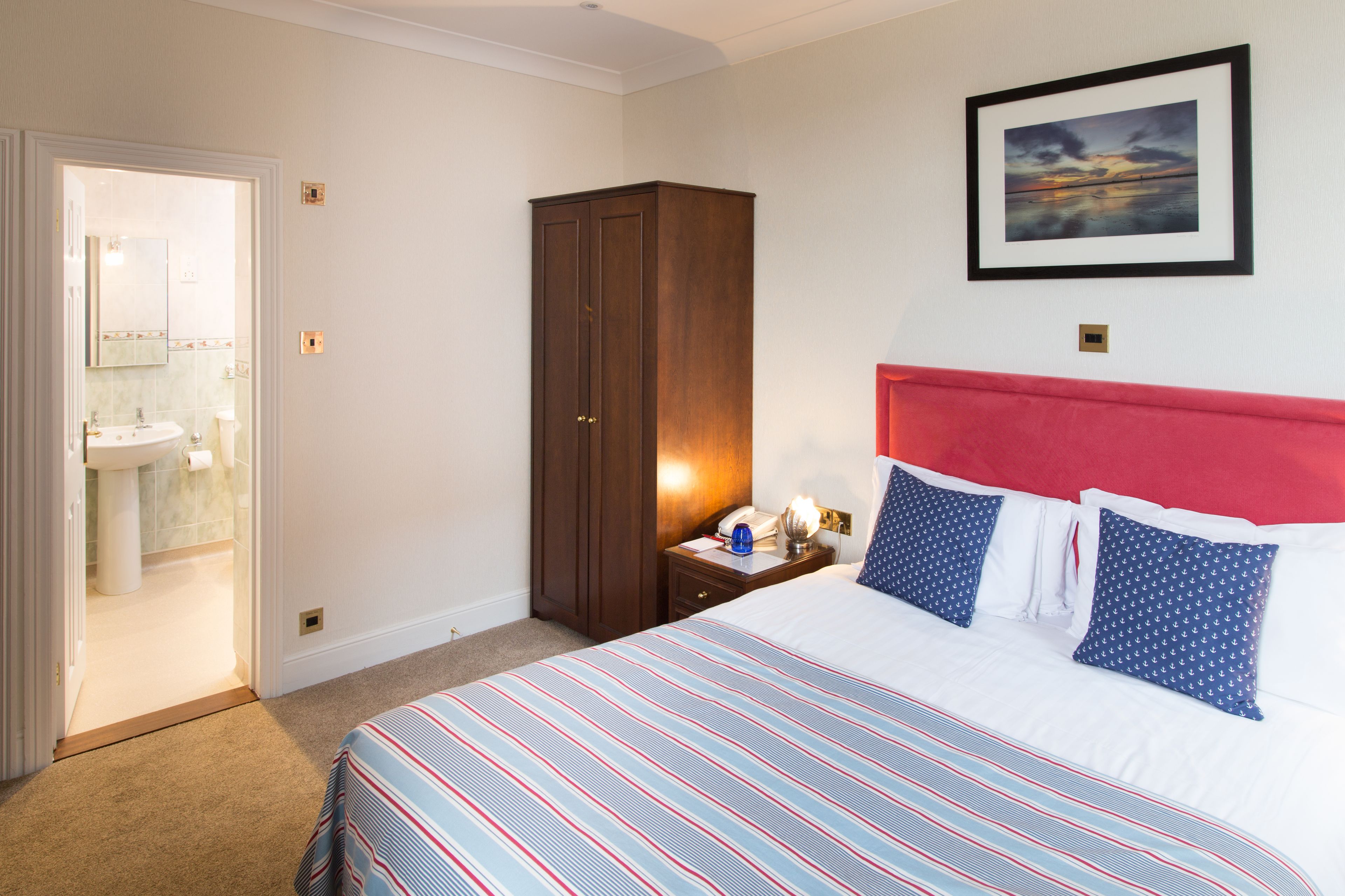 A hotel room with a bed, a nightstand, a wardrobe, and a bathroom visible through an open door.