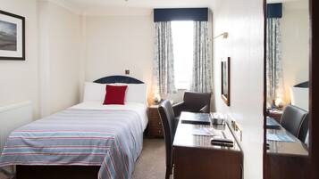 Habitació d'hotel amb un llit, escriptori i una cadira. Hi ha una finestra amb cortines, una làmpada a l'escriptori i un quadre amb marc a la paret.