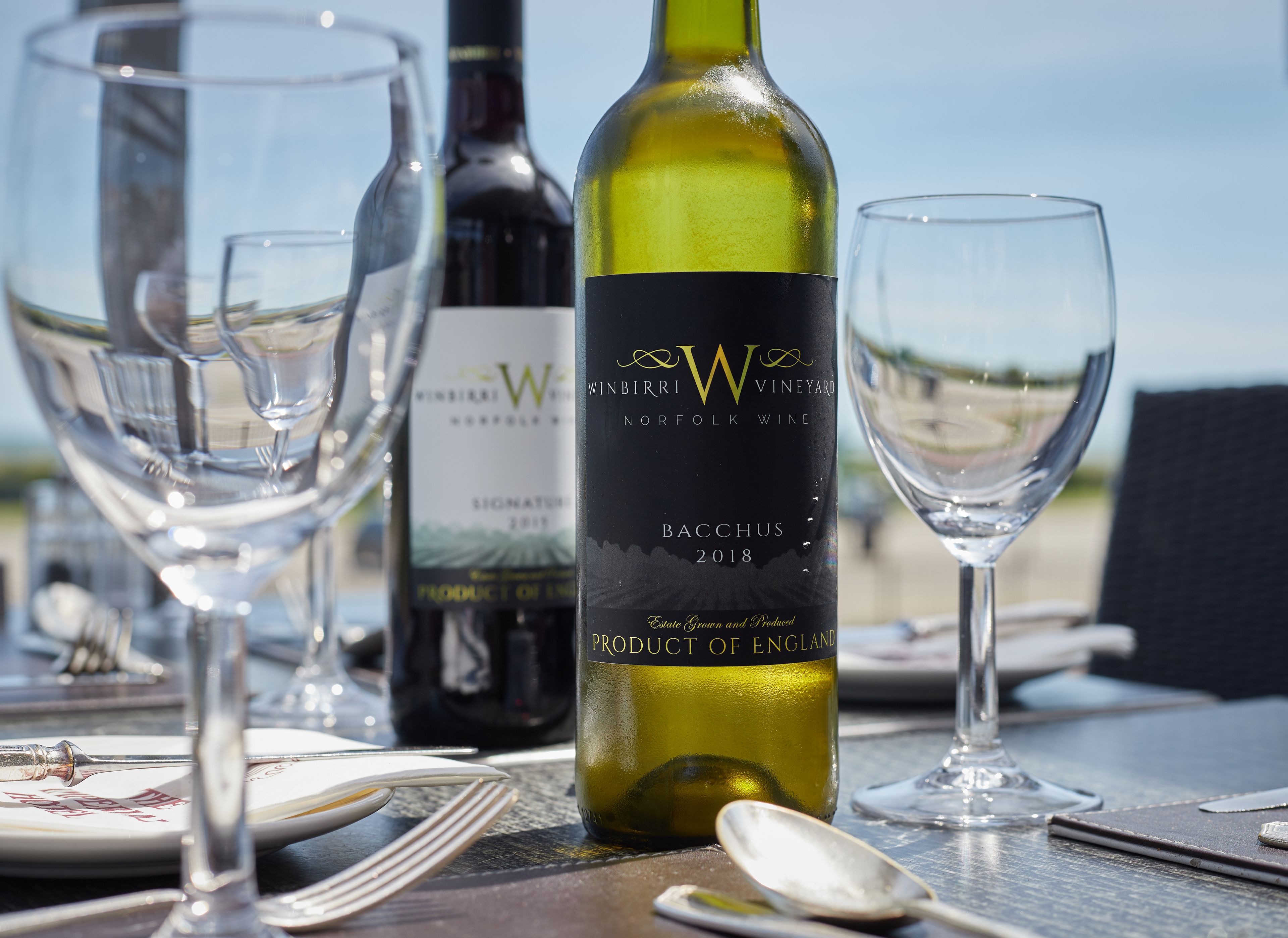 A table set with wine glasses, a bottle of wine, and a spoon.