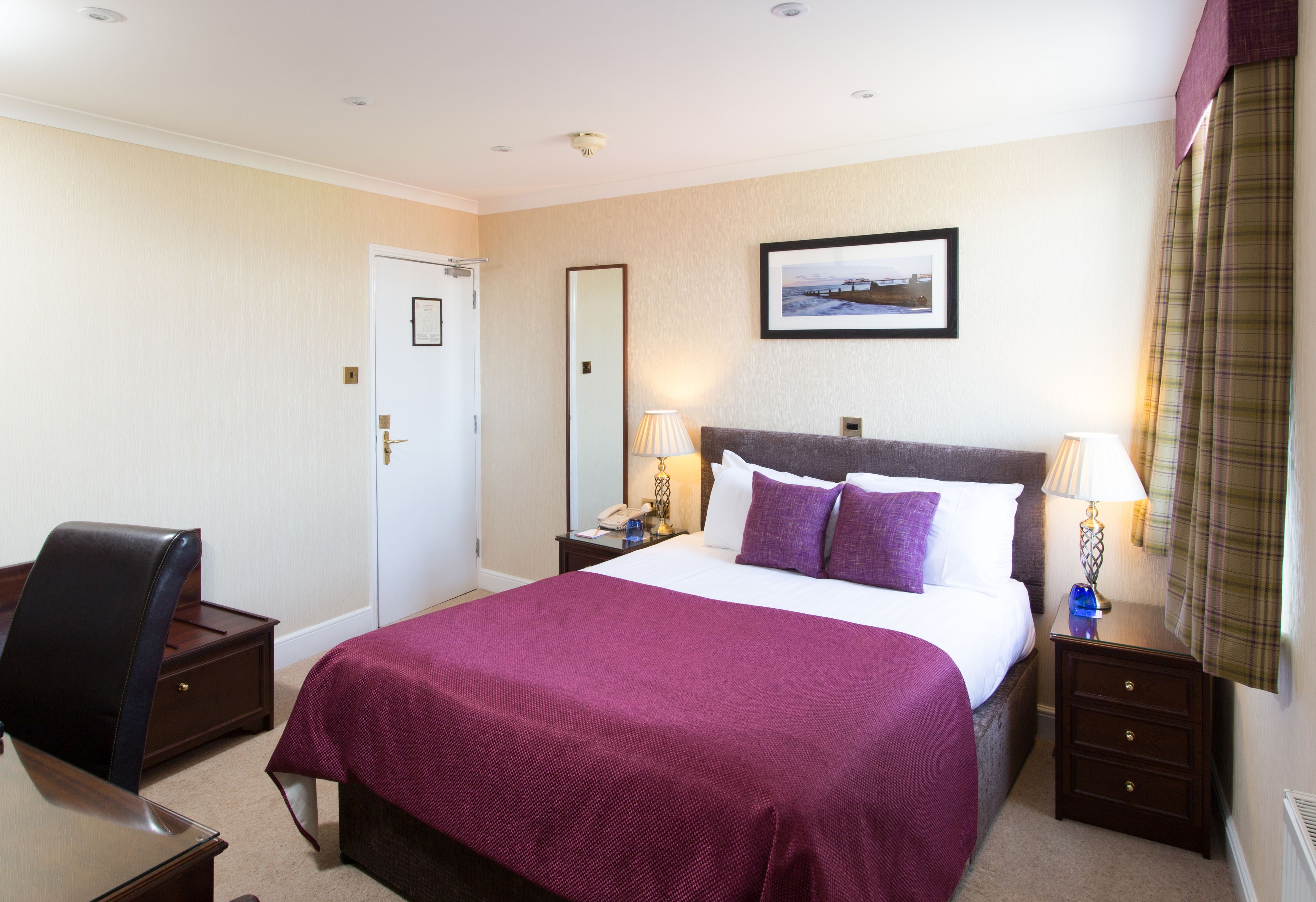 A hotel room with a large bed, two bedside tables, a chair, a desk, and a door.