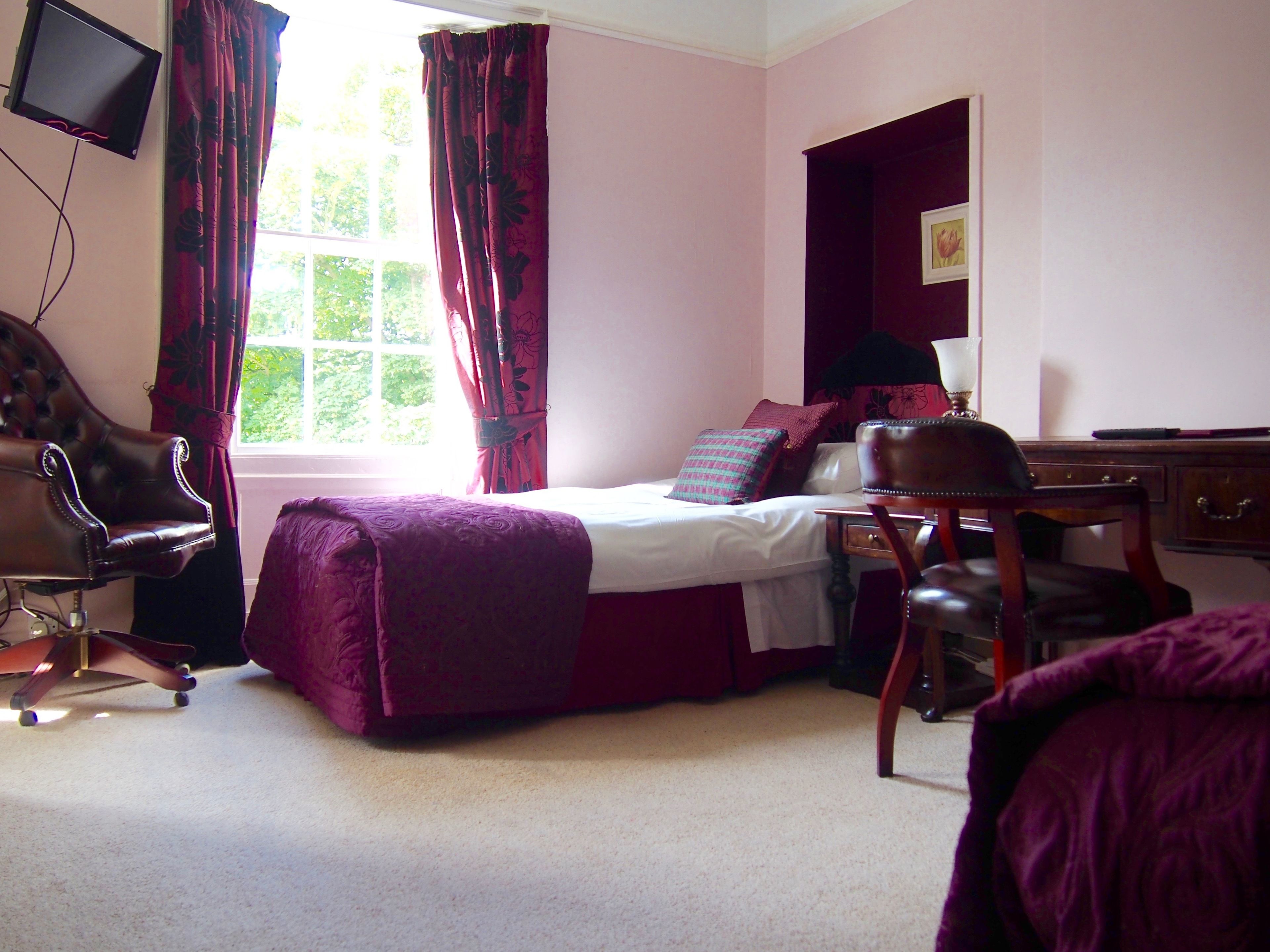 A bedroom with a bed, a desk, a chair, a television, and a window with curtains.