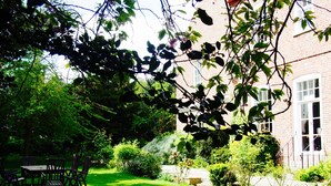 Un jardin bien entretenu, avec un bâtiment en briques, une table et des chaises en bois, et un chemin en pierre.