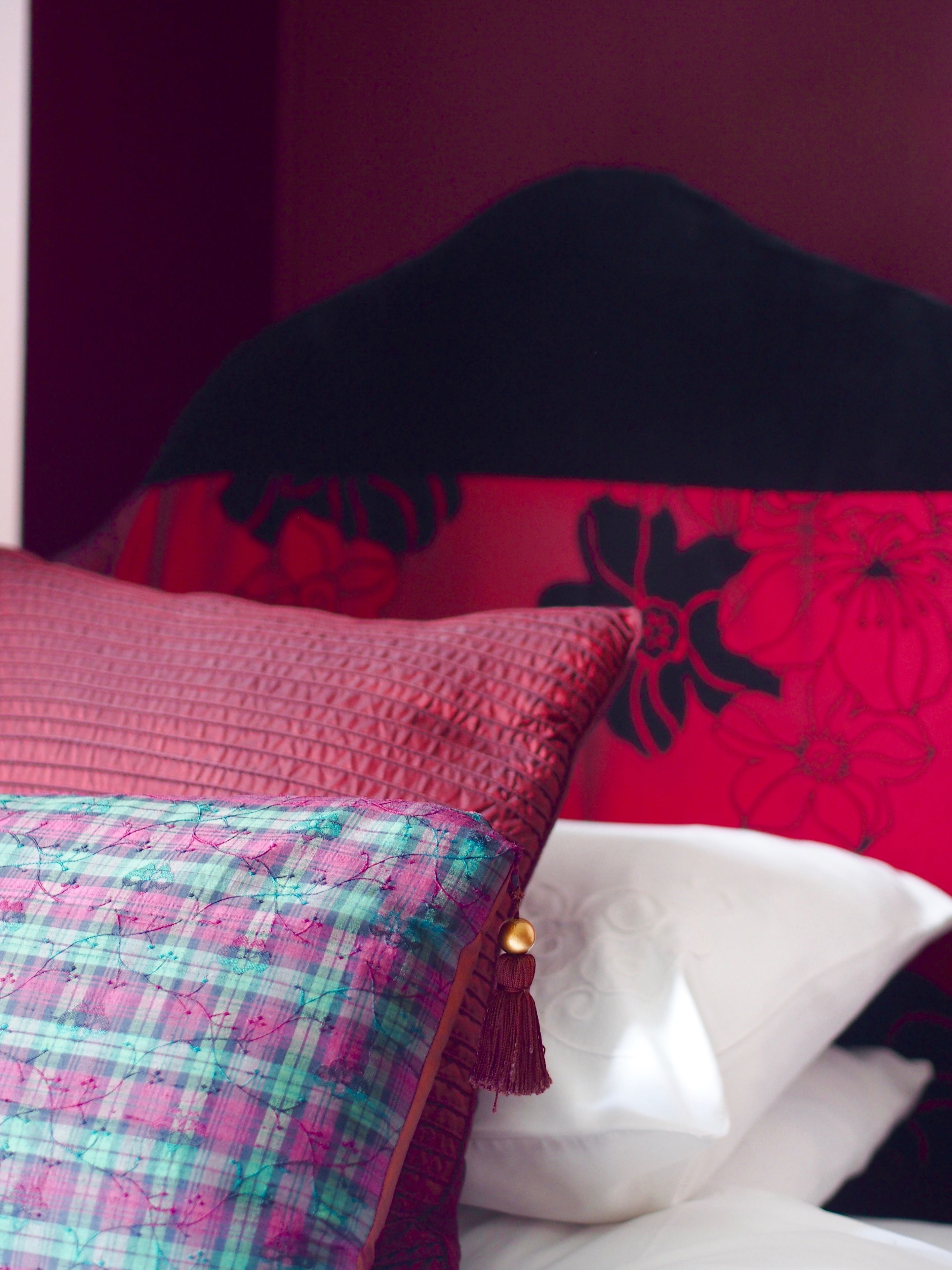 A bed with a red and black floral pillow, a plaid pillow, and a white pillow.