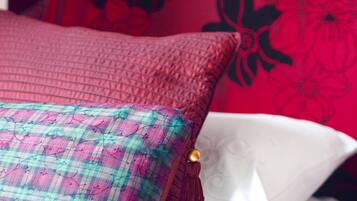 A bed with a red and black floral pillow, a plaid pillow, and a white pillow.